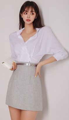 Woman in a white shirt and grey skirt holding a white quilted bag