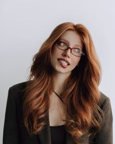 Woman with long red hair and glasses biting her lip, looking to the side