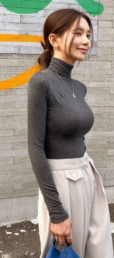 Woman in a gray turtleneck and light pants standing outdoors