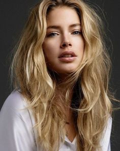 Woman with long blonde wavy hair wearing a white shirt against a dark background