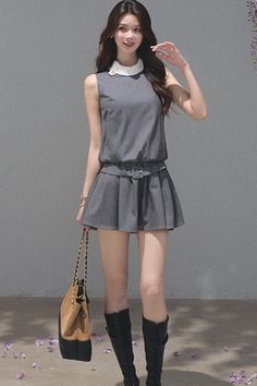 Woman in a gray dress with a white collar and black boots holding a handbag