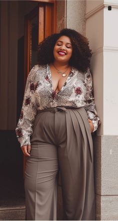 Woman with curly hair and a floral blouse leaning against a wall