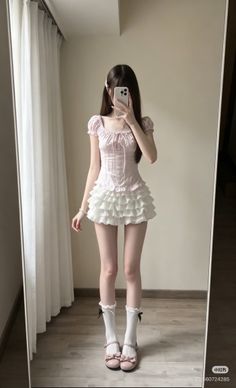 Person in a pink top and white ruffle skirt taking a mirror selfie