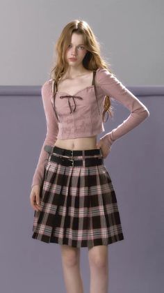 Woman with long hair wearing a pink crop top and plaid skirt with double belt