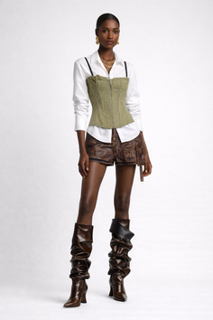 Woman in a white shirt, corset top, leather shorts, and tall boots