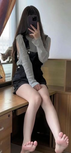 Person in overalls sitting on a desk with a cat nearby