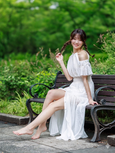 Woman in a white dress with braids sitting barefoot on a park bench