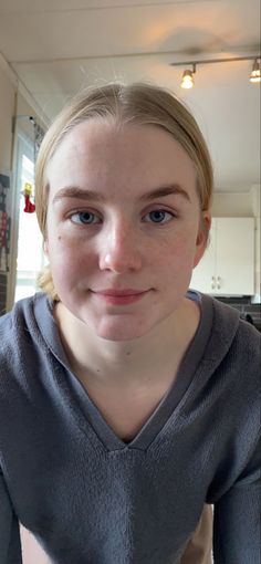 Young woman with blonde hair and blue eyes wearing a grey hoodie indoors