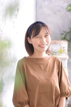 Woman with short hair and a headband smiling in a brown shirt indoors