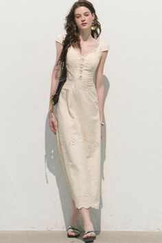Woman in a cream dress with long hair standing against a white wall