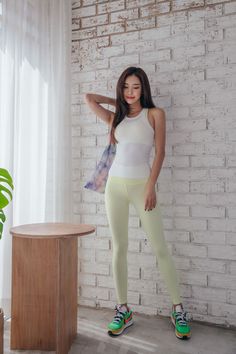 Woman in a white tank top and yellow leggings posing indoors