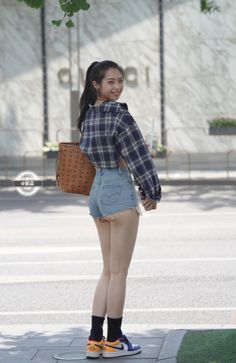 Woman in denim shorts and plaid shirt looking back over her shoulder on a street