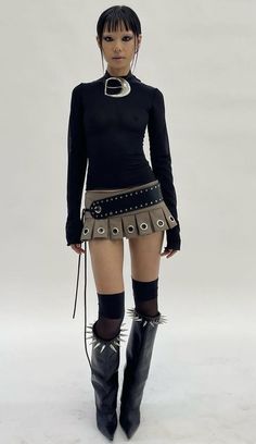 Woman in a black top, mini skirt, and spiked boots posing in a studio