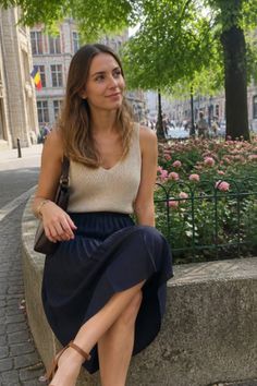 Woman with long hair sitting on a stone ledge on a city street with pink flowers