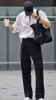 Person in a white shirt and black pants holding a coffee cup and tote bag