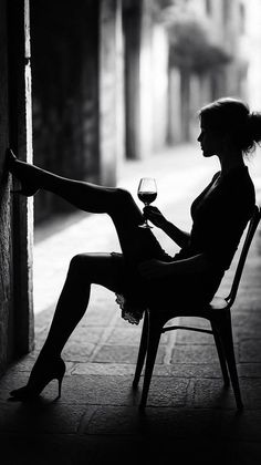 Woman in silhouette holding a wine glass, with one leg raised against a wall