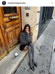 Woman in a gray sweater and mini skirt sitting on a sidewalk