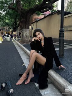 Woman in a black dress and sheer stockings sitting on a street curb at night
