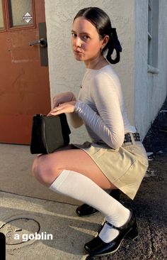 Woman with dark hair in a mini skirt and knee-high socks squatting outdoors
