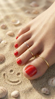 Foot with red nail polish and toe rings on a sandy beach with seashells