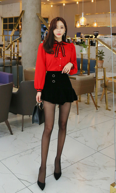Woman in a red blouse and black skirt with pantyhose and high heels indoors