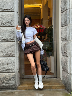 Woman in a white crop top and brown mini skirt holding a coffee cup outdoors
