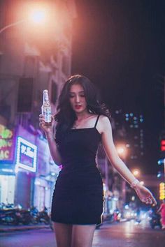 Woman in a black dress holding a bottle on a neon-lit street at night