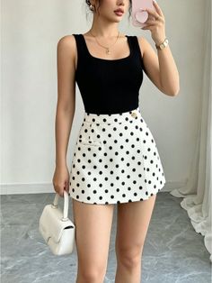 Woman in a black tank top and polka dot skirt holding a white handbag