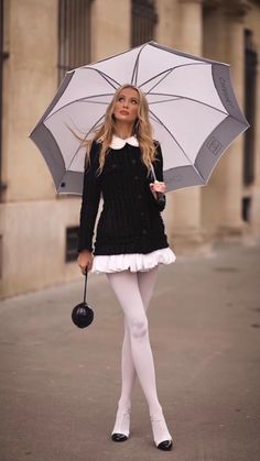 Woman in a black jacket with a white collar and white tights holding an umbrella
