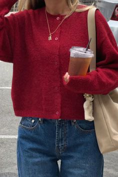 Person in a red cardigan and blue jeans holding an iced tea