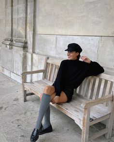 Woman in a black sweater and shorts with knee-high socks sitting on a bench