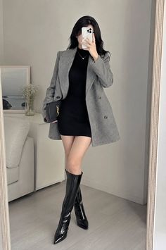 Woman in a black dress and gray blazer taking a mirror selfie