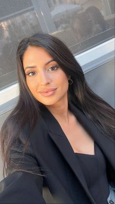 Woman with long black hair wearing a black blazer and hoop earrings