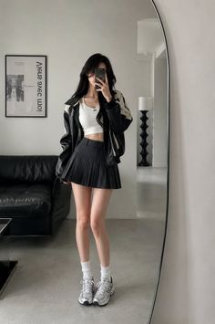 Woman in a pleated skirt and crop top taking a mirror selfie indoors