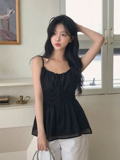 Woman with long black hair wearing a black top and white pants indoors