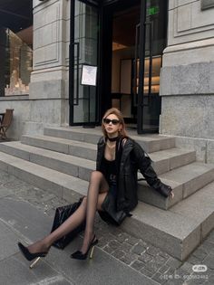 Woman in a black leather jacket and sunglasses sitting on stone steps outdoors
