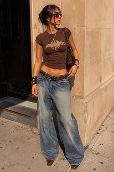 Woman in a brown crop top and baggy jeans standing outdoors in golden hour light