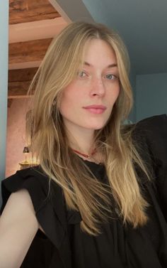Woman with blonde hair and blue eyes wearing a black top and red choker indoors