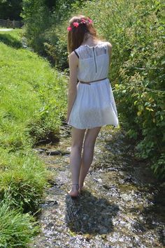 Woman in a white dress and flower crown walking barefoot in a stream