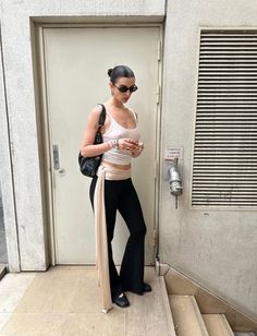 Woman in a white tank top and black pants standing outdoors