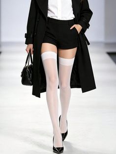Person in white thigh highs, black shorts, and a trench coat on a runway