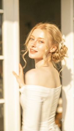 Blonde woman in an off-shoulder top with an updo, smiling over her shoulder