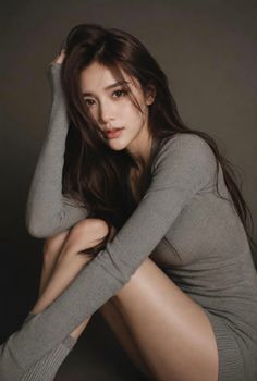 Woman with long brown hair in a gray dress, sitting with exposed legs