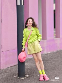 Woman in a lime green sweater and shorts with pink accessories, smiling outdoors