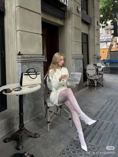 Woman with blonde hair in a white outfit and lace tights sitting at an outdoor cafe