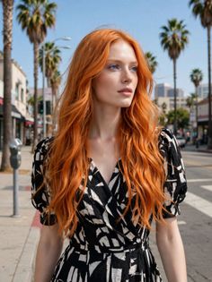 Woman with long red hair and blue eyes in a black and white dress on a street with palm trees