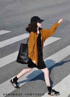 Woman in a black dress and oversized shirt crossing a street