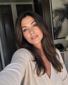 Woman with long brown hair wearing a cream sweater and gold necklace indoors