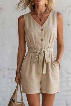 Woman in a beige sleeveless jumpsuit with a belted waist and layered necklaces