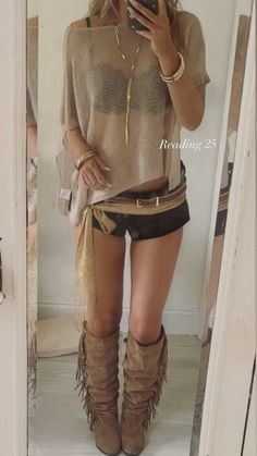 Woman in a sheer top, black shorts, and fringe boots taking a mirror selfie